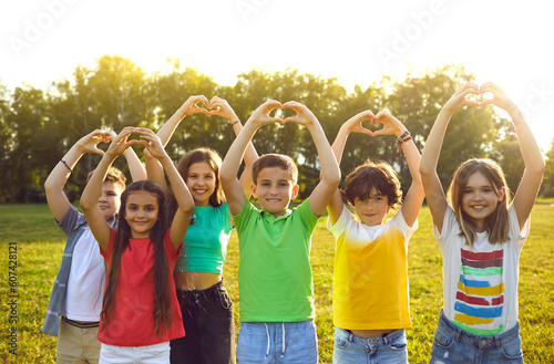 Happy children wish for world peace. Cheerful healthy kids standing on camp field or park lawn in sunset or sunrise sunlight look at camera, smile, raise hands up and do heart gestures. Group portrait