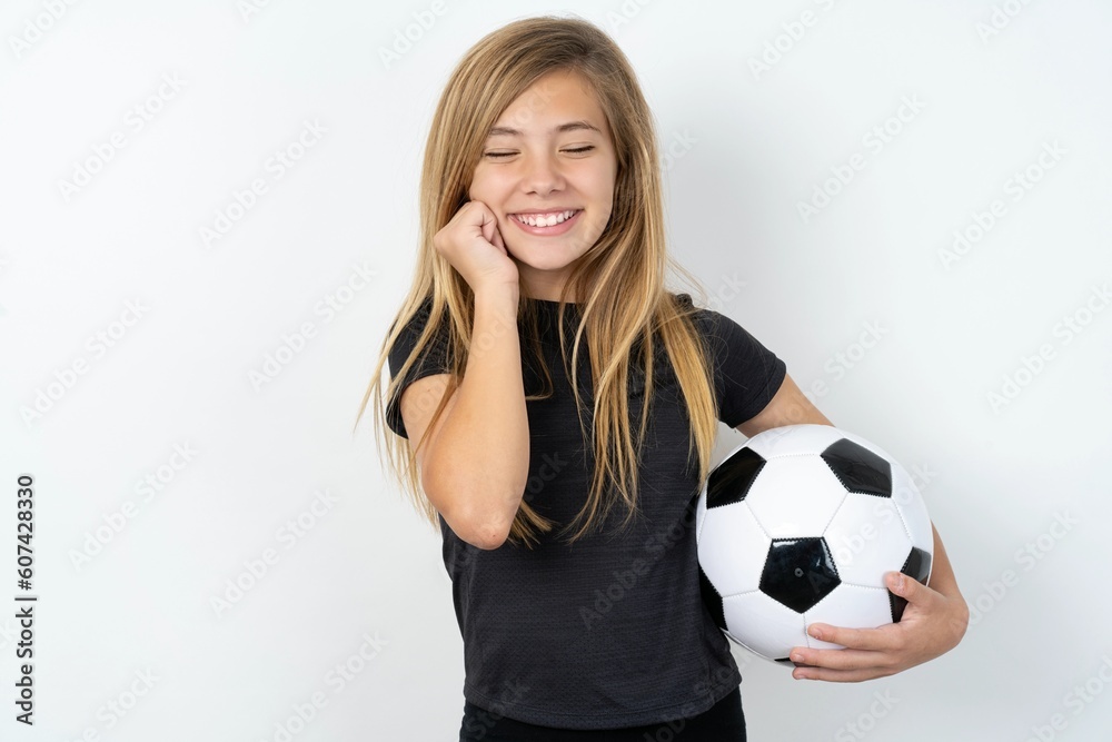 beautiful caucasian teen girl wearing sportswear  over white wall grins joyfully, imagines something pleasant, copy space. Pleasant emotions concept.