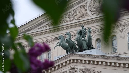 Quadriga sculpture on facade of Bolshoi Theatre building in Moscow in the background. Blurred purple lilac flowers in the foreground. Soft focus. Handheld video. Russian culture theme.