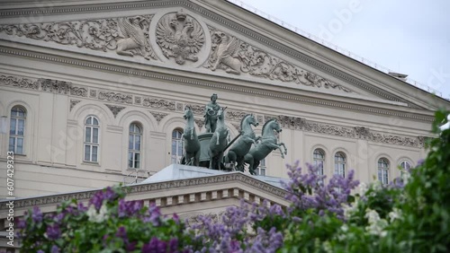 Quadriga sculpture on facade of Bolshoi Theatre building in Moscow in the background. Blurred purple lilac flowers in the foreground. Soft focus. Handheld video. Russian culture theme.