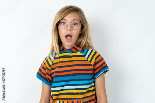 Expressive facial expressions. Shocked stupefied beautiful caucasian teen girl wearing striped T-shirt over white wall, keeps jaw dropped feels stunned from what he sees aside. © Jihan
