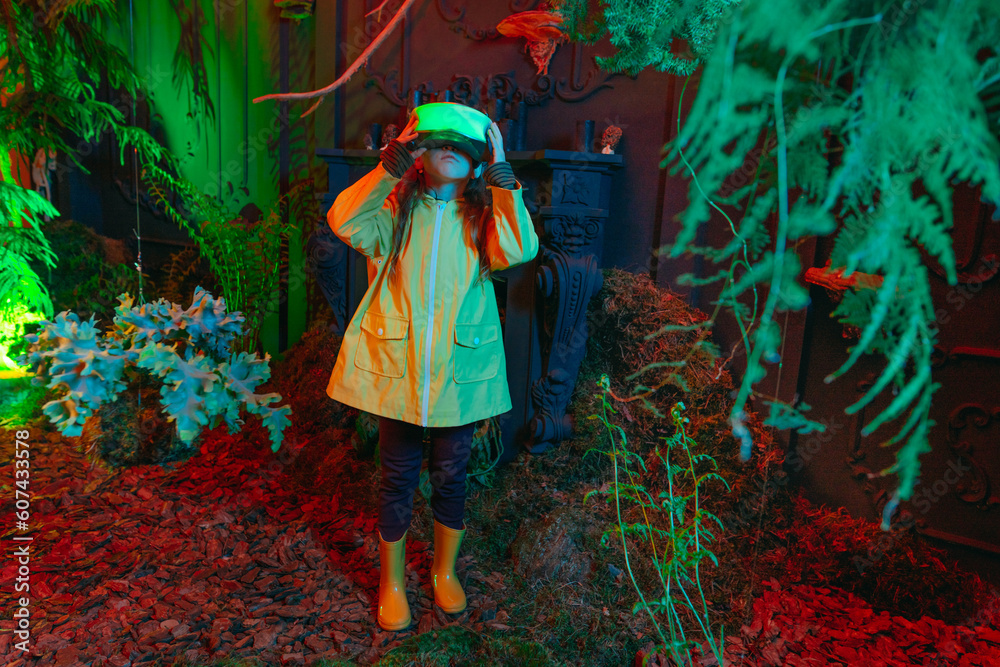 Little girl in luminous VR glasses standing in room with plants in neon lights Little girl in luminous VR glasses standing in room with plants in neon lights