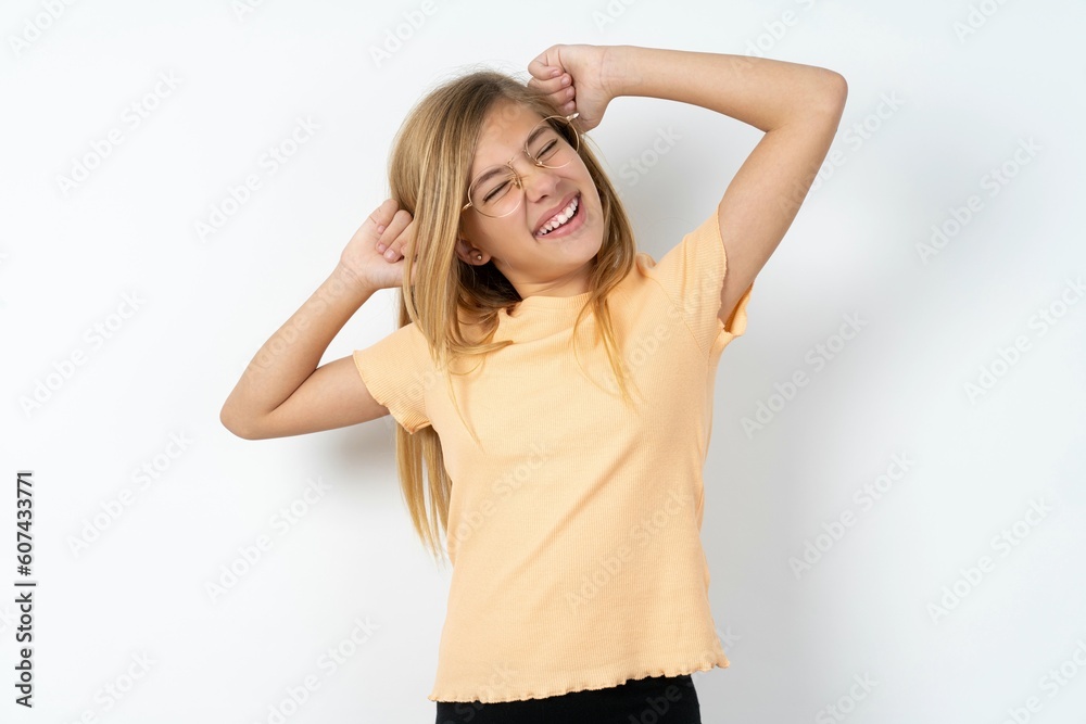 beautiful caucasian teen girl wearing orange T-shirt over white wall relaxing and stretching, arms and hands behind head and neck smiling happy beautiful caucasian teen girl wearing orange T-shirt over white wall relaxing and stretching, arms and hands behind head and neck smiling happy