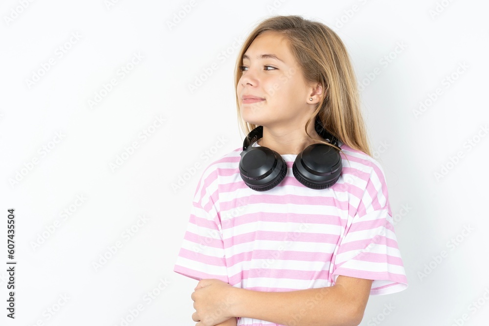 Fototapeta premium Self confident serious calm beautiful caucasian teen girl wearing striped T-shirt over white wall stands with arms folded. Shows professional vibe stands in assertive pose.
