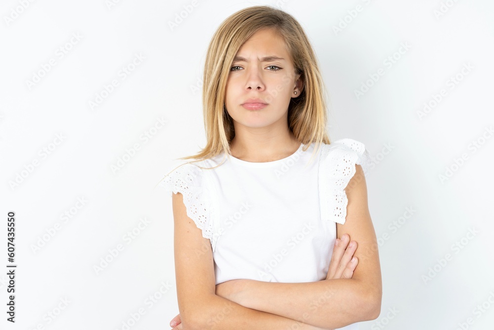 Gloomy dissatisfied beautiful caucasian teen girl wearing white T-shirt over white wall looks with miserable expression at camera from under forehead, makes unhappy grimace Gloomy dissatisfied beautiful caucasian teen girl wearing white T-shirt over white wall looks with miserable expression at camera from under forehead, makes unhappy grimace
