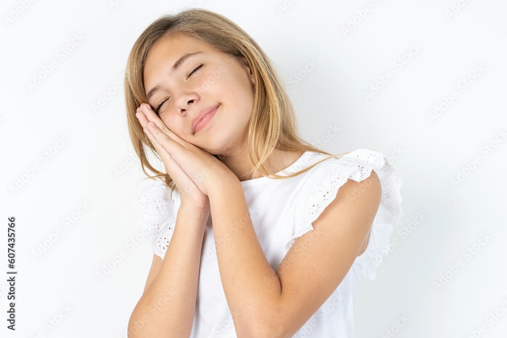 beautiful caucasian teen girl wearing white T-shirt over white wall leans on pressed palms closes eyes and has pleasant smile dreams about something beautiful caucasian teen girl wearing white T-shirt over white wall leans on pressed palms closes eyes and has pleasant smile dreams about something