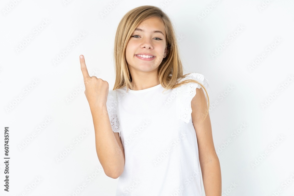 beautiful caucasian teen girl wearing white T-shirt over white wall smiling and looking friendly, showing number one or first with hand forward, counting down beautiful caucasian teen girl wearing white T-shirt over white wall smiling and looking friendly, showing number one or first with hand forward, counting down