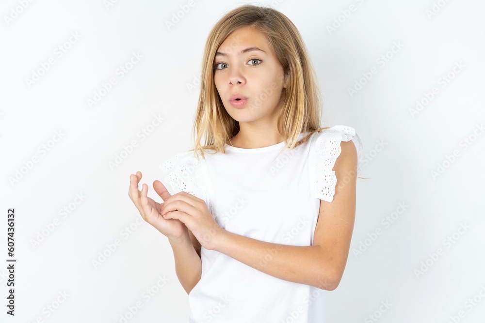 Surprised emotional beautiful caucasian teen girl wearing white T-shirt over white wall rubs palms and stares at camera with disbelief Surprised emotional beautiful caucasian teen girl wearing white T-shirt over white wall rubs palms and stares at camera with disbelief