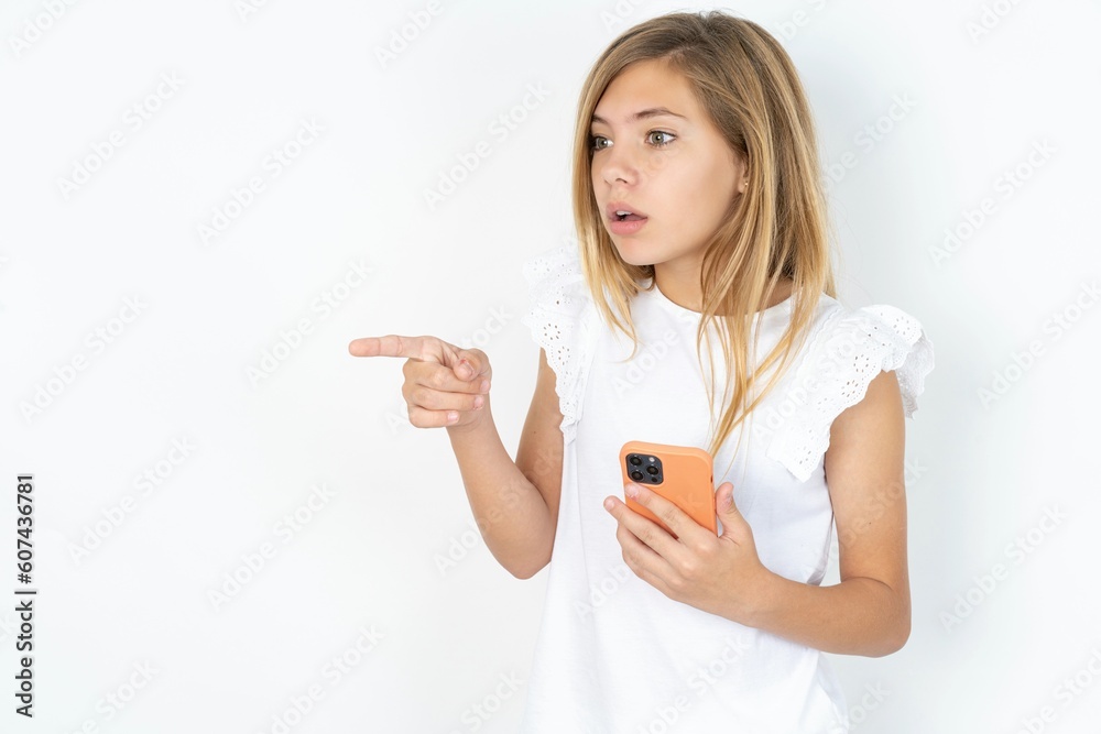 Stunned beautiful caucasian teen girl wearing white T-shirt over white wall points sideways right copy space, recommends product, sees astonishing thing Stunned beautiful caucasian teen girl wearing white T-shirt over white wall points sideways right copy space, recommends product, sees astonishing thing