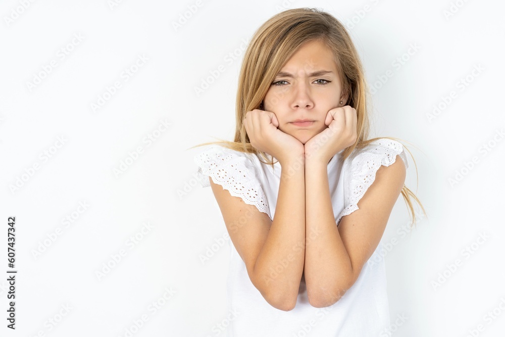 Portrait of sad beautiful caucasian teen girl wearing white T-shirt over white wall hands face Portrait of sad beautiful caucasian teen girl wearing white T-shirt over white wall hands face