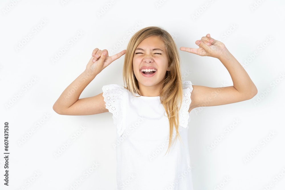 Photo of crazy beautiful caucasian teen girl wearing white T-shirt over white wall screaming and pointing with fingers at hair closed eyes Photo of crazy beautiful caucasian teen girl wearing white T-shirt over white wall screaming and pointing with fingers at hair closed eyes