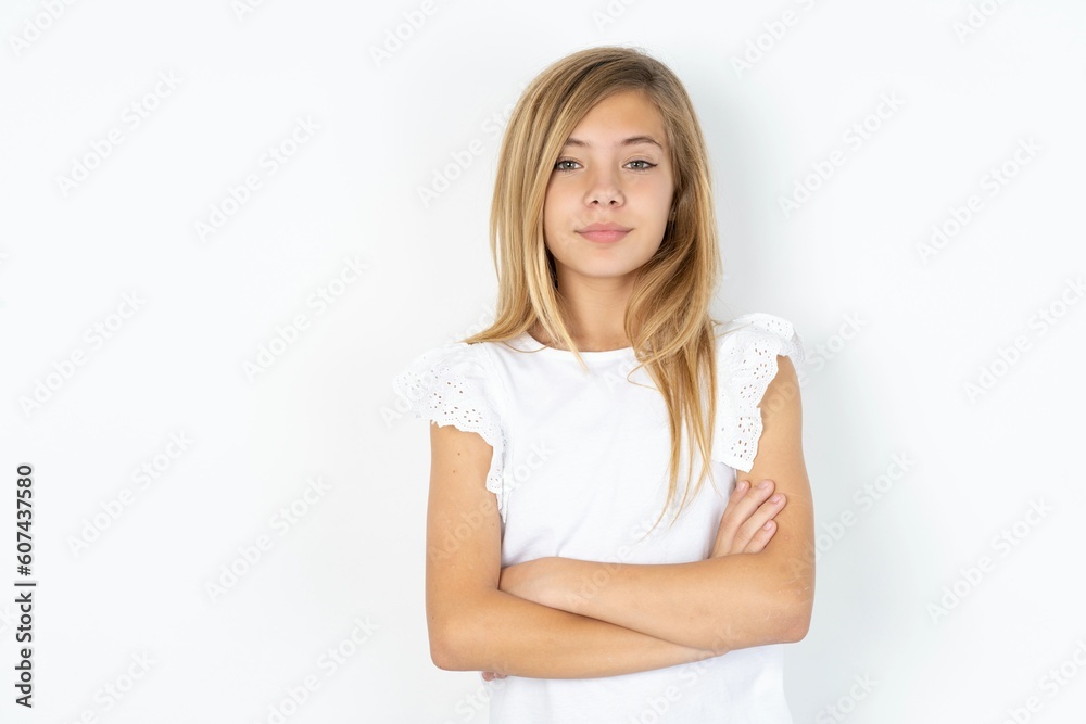 Confident beautiful caucasian teen girl wearing white T-shirt over white wall with arms crossed looking to the camera Confident beautiful caucasian teen girl wearing white T-shirt over white wall with arms crossed looking to the camera