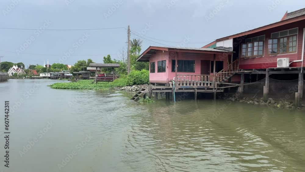 Sailing on boat towards canal slowly with view of traditional wooden Thai homes on waterfront. Point of view shot daytime. Nature concept. Thailand