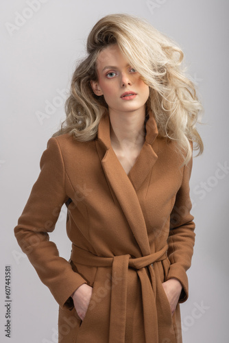 Beauty, fashion and make-up concept. Beautiful blonde woman with big wavy hair close-up studio portrait. Model with pink make-up wearing garment coat and looking at camera with seductive look