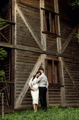 beautiful pregnant couple on the background of a wooden ecological house in the forest. a man hugs a pregnant woman.