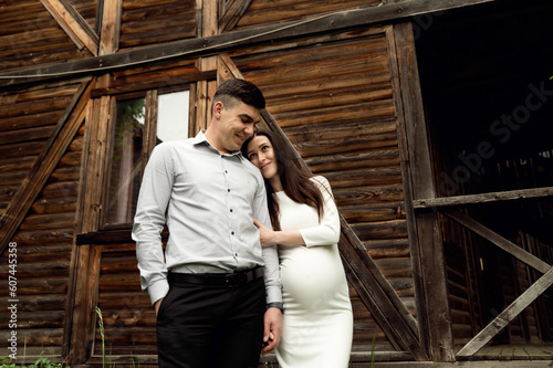 beautiful pregnant couple on the background of a wooden ecological house in the forest. a man hugs a pregnant woman. © Vadym