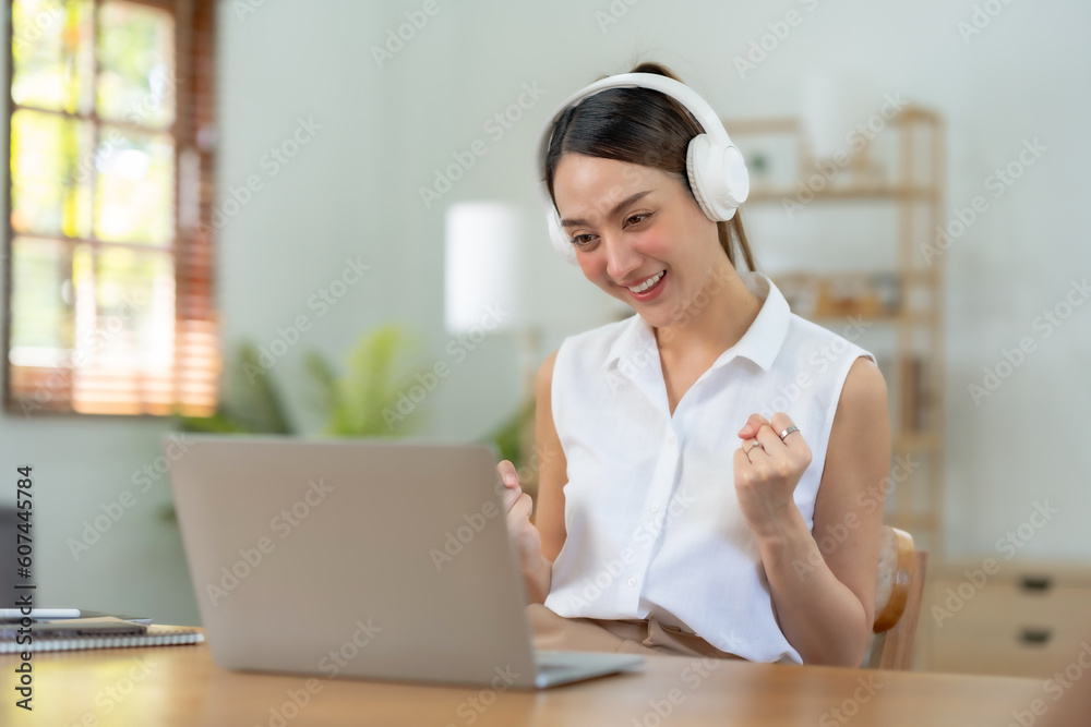 Obraz premium Happy young Asian woman raising hands with victory smiling happily with laptop computer at home. The concept of success at work.