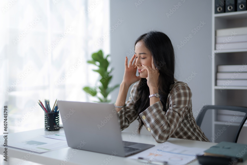Young Asian businesswoman worried about problem at work and stressed with laptop computer at office.