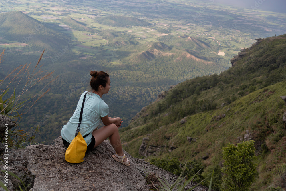 Naklejka premium Hiking woman in relaxing on the cliff looking at a beautiful sunlit landscape. Green valley in sunligh