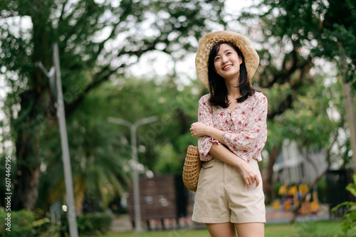 Portrait of asian young woman traveler with weaving hat and basket happy smile on green public park nature background. Journey trip lifestyle, world travel explorer or Asia summer tourism concept.