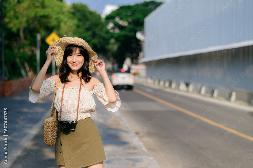Portrait of asian young woman traveler with weaving hat and basket and a camera on green public park nature background. Journey trip lifestyle, world travel explorer or Asia summer tourism concept.