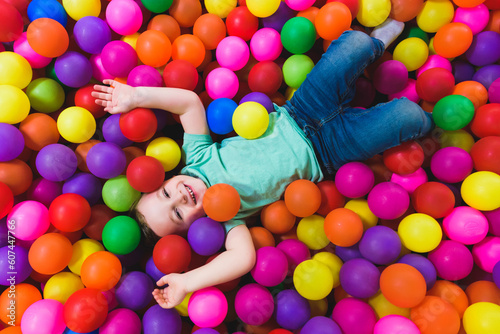 Smiling boy playing lying on colorful balls in the park