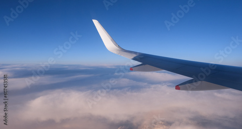 Airplane in flight. People travelling. Aerial view from plane window. Blue sky above clouds