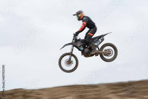 Unrecognized athlete riding a sports motorbike jumping on the air on a motocross race. Fast speed extreme sport.