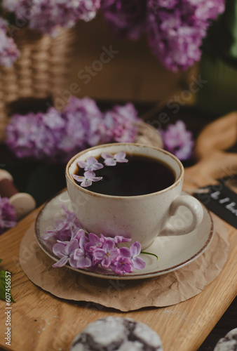 A cup of Americano black coffee, purple lilac flowers on a wooden background. A cup of Americano black coffee, purple lilac flowers on a wooden background. Lilac inscription on the card next to it