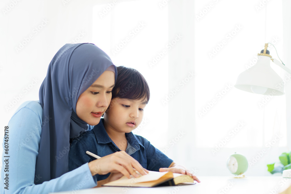 Happy cheerful Asian muslim woman woman teaching her little son a drawing on digital tablet. Happy cheerful Asian muslim woman woman teaching her little son a drawing on digital tablet.