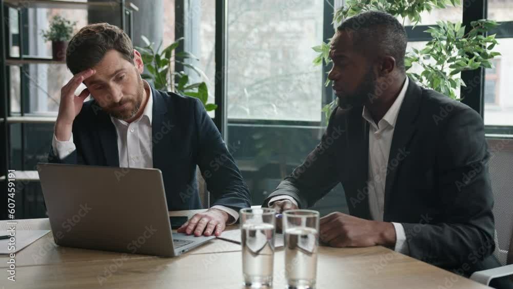 Two diverse workers men multiracial partners office coworkers businessmen with papers and laptop sad upset business failure discuss computer project difficulties startup marketing result data problem