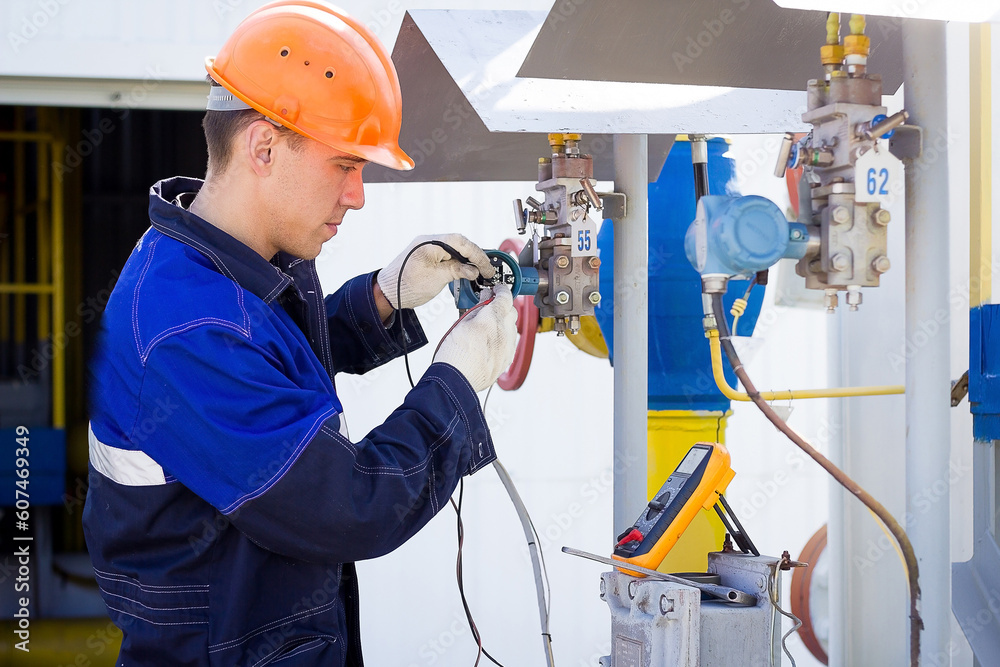 Instrumentation and control engineer diagnoses the operation of gas distribution station equipment on a summer day. A professional worker in a hard hat and overalls diagnoses gas equipment sensors Instrumentation and control engineer diagnoses the operation of gas distribution station equipment on a summer day. A professional worker in a hard hat and overalls diagnoses gas equipment sensors