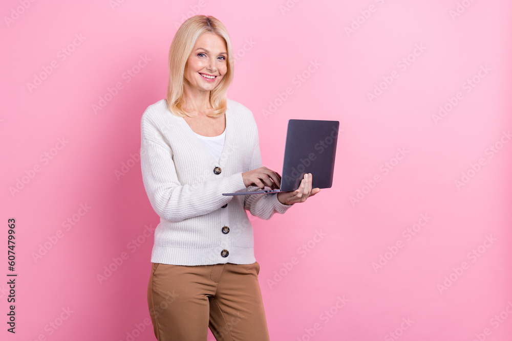 Photo of positive aged lady recruiter use wireless netbook empty space isolated on pink color background Photo of positive aged lady recruiter use wireless netbook empty space isolated on pink color background