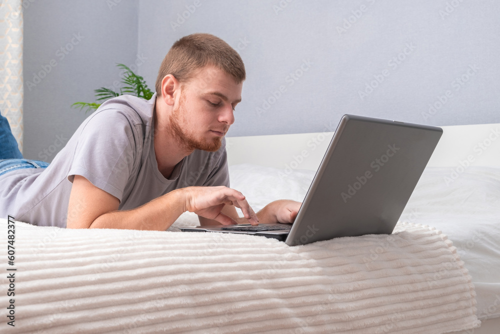 A man with laptop is lying in bed. Freelancer works remotely from home. Distance education. Online shopping without leaving home. Internet surfing. Gambling addiction. Black Friday sale. Cyber Monday. A man with laptop is lying in bed. Freelancer works remotely from home. Distance education. Online shopping without leaving home. Internet surfing. Gambling addiction. Black Friday sale. Cyber Monday.