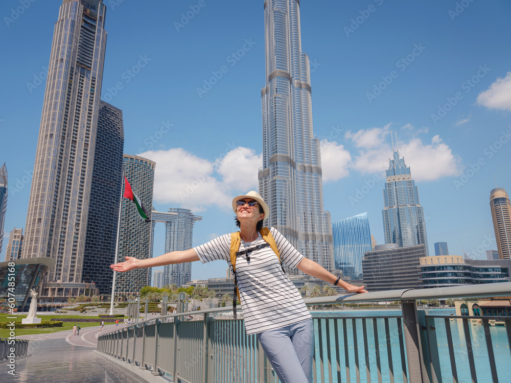 Enjoying travel in United Arabian Emirates. Young woman with yellow backpack walking on Dubai Downtown in sunny summer day. Enjoying travel in United Arabian Emirates. Young woman with yellow backpack walking on Dubai Downtown in sunny summer day.