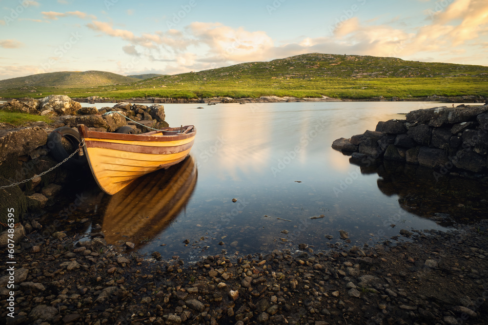 Obraz premium Beautiful morning landscape scenery with old wooden fishing boat reflected in lake with mountains in the background at Screebe, connemara national Park in County Galway, Ireland 