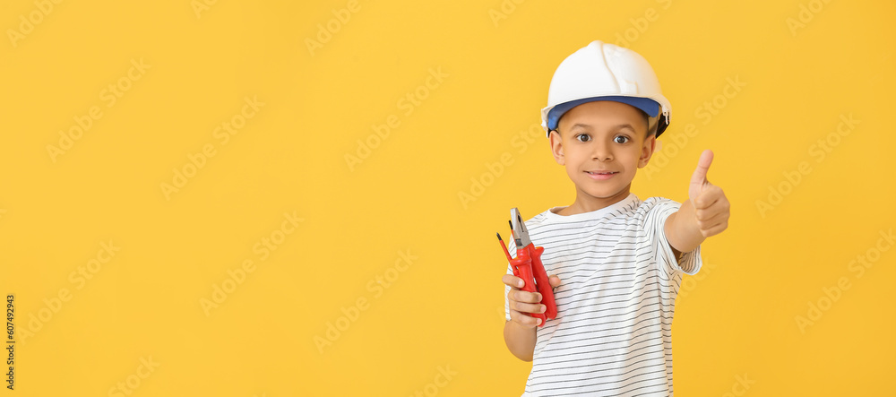 Little African-American electrician with tools showing thumb-up gesture on yellow background with space for text Little African-American electrician with tools showing thumb-up gesture on yellow background with space for text