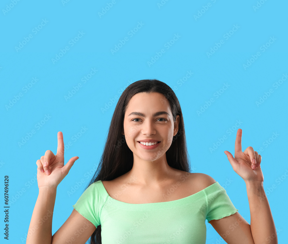 Beautiful young woman pointing at something on blue background, closeup Beautiful young woman pointing at something on blue background, closeup