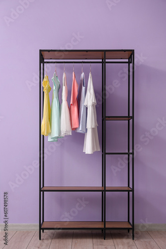 Shelving unit with children's dresses near lilac wall in room © Pixel-Shot
