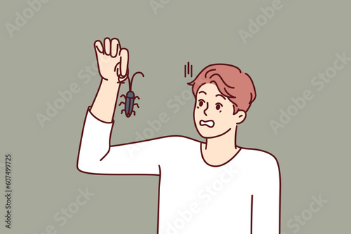Man with bug in hand, looks at insect and gets scared suffering from arachnophobia and disgust. Guy found bug and wants to get rid of pest by calling service for chemical treatment of insects