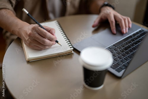Close-up shot of male hand holding a pencil to write something on a notebook. Freelance work at cafe.