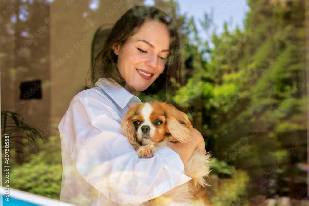 Smiling young woman holding her puppy in her hand and standing behind the glass window Smiling young woman holding her puppy in her hand and standing behind the glass window