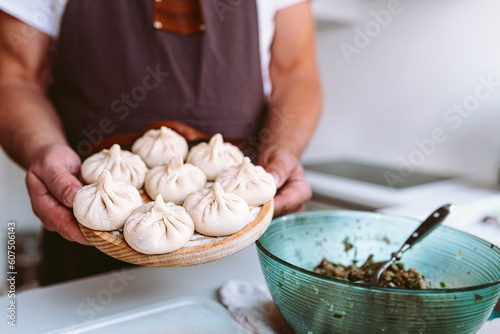 hands cook hold round wooden board with floured, handmade khinkali