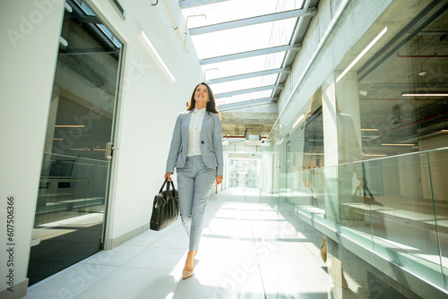 Pretty young business woman walking with briefcase in the office hallway