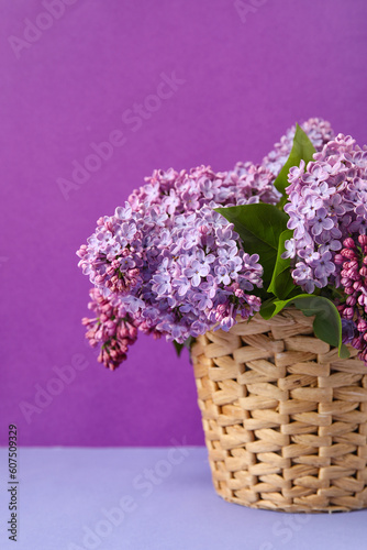 Wicker basket with blooming lilac branches on color background