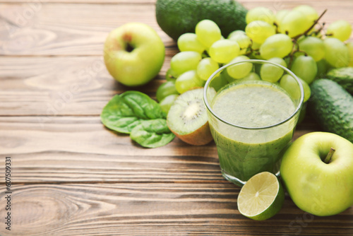 Green smoothie in glass with fruits and vegetables on brown wooden background