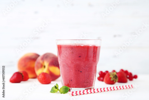Red smoothie in glass with fruits on white wooden background