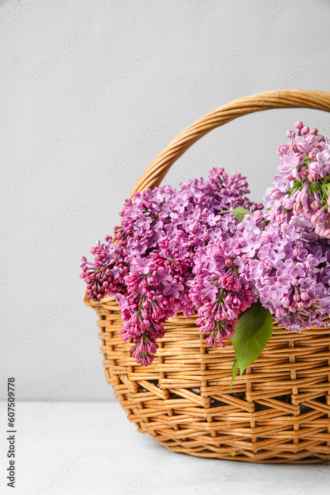 Wicker basket with aromatic lilac flowers on light table, closeup