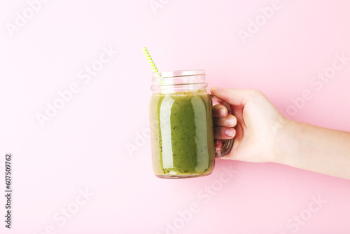 Female hand holding glass jar with green smoothie on pink background
