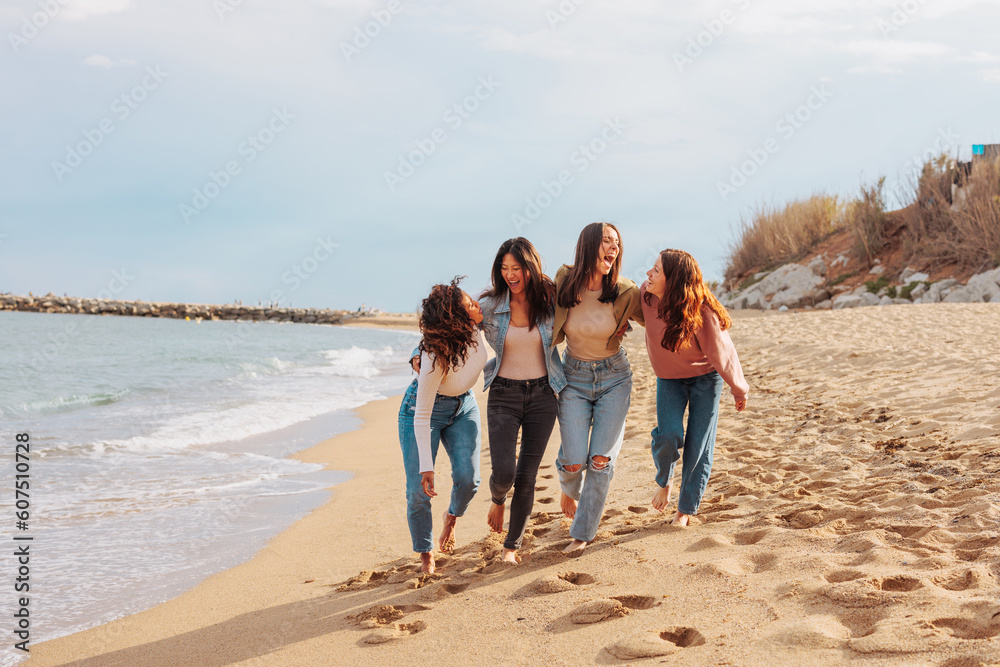 Four diverse young women walking on empty beach